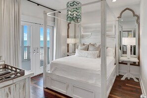 Una cama con dosel, lámparas de noche y vista al océano a través de una puerta.