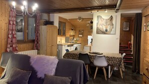 A cozy room with a bed, a dining table with chairs, a kitchen area, and a wooden ceiling.