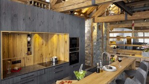 A modern kitchen with wooden beams, a stone wall, and a wooden countertop. - Chalet, wifi, 150m from ski slopes, sauna, terrace, fireplace or stove, tv, 260m², Les 2 Alpes (Les Deux Alpes)