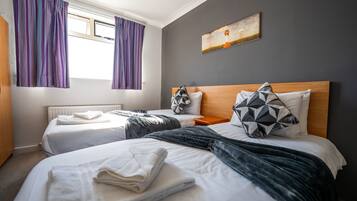 A hotel room with two beds, a wooden headboard, a painting on the wall, and purple curtains.