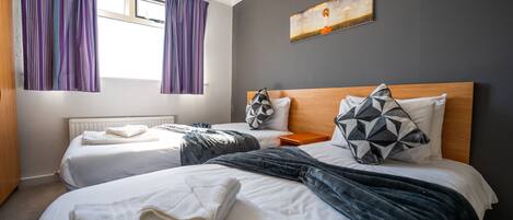 A hotel room with two beds, a wooden headboard, a painting on the wall, and purple curtains.