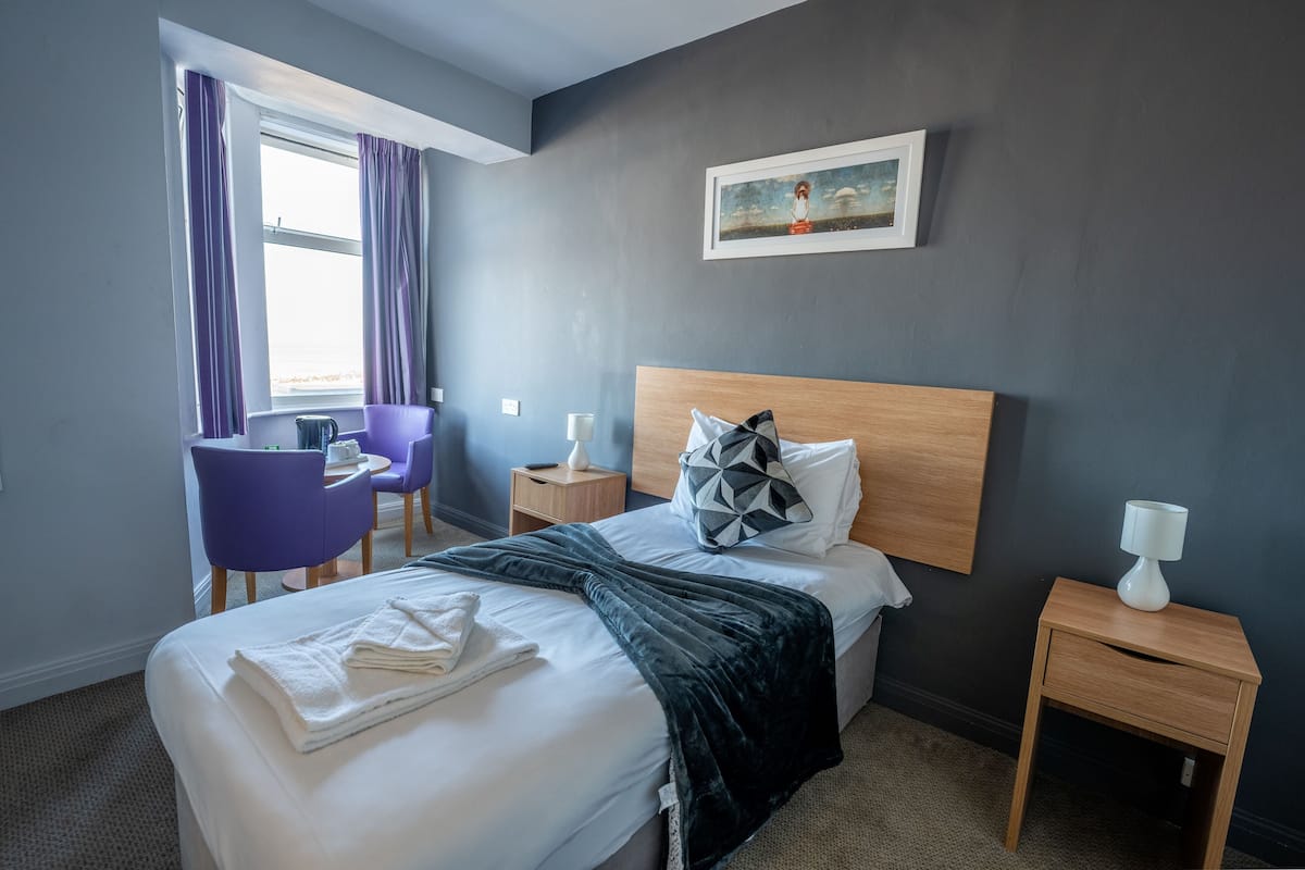 Habitación de hotel con cama, escritorio, silla, mesita de noche y un cuadro en la pared.