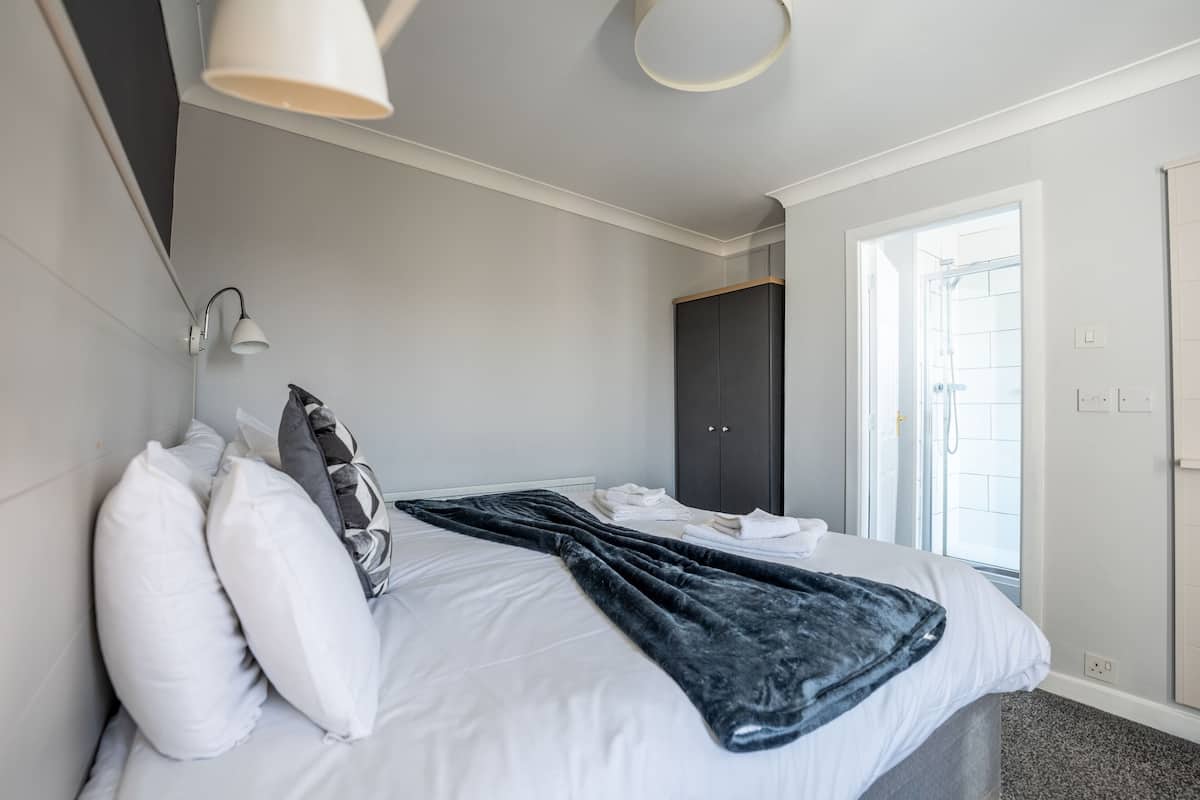 Un dormitorio moderno con cama, almohadas blancas, una manta oscura, un armario y una ventana.