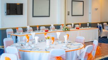 A conference room with a long table, white chairs with orange sashes, and a white tablecloth.