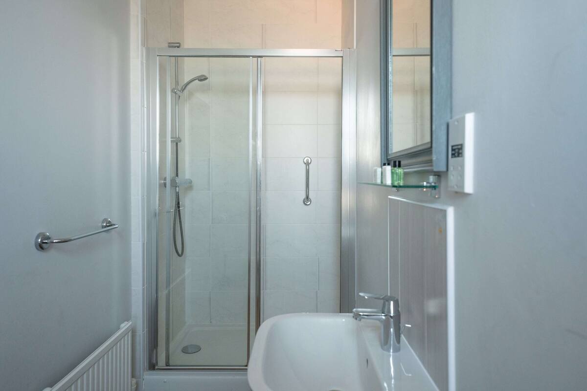 Un baño moderno con ducha de vidrio, un lavamanos blanco y un espejo encima.