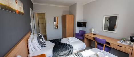 A hotel room with two beds, a desk, a chair, a TV, and a wardrobe.