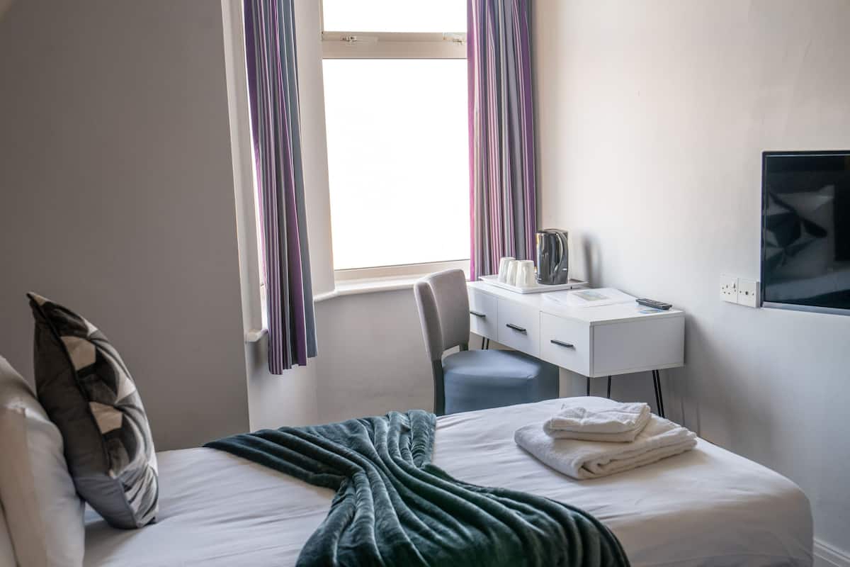 Habitación de hotel con cama, escritorio, silla, televisor y ventana con cortinas.