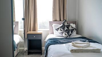 A neatly made bed with a geometric pillow, a bedside table, and a window with curtains.