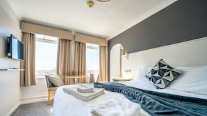A hotel room with a bed, a TV, a desk, and a window with curtains.