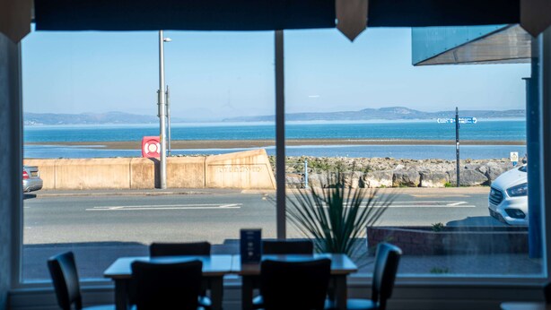 A view from inside a room with a large window overlooking a beach and the ocean.