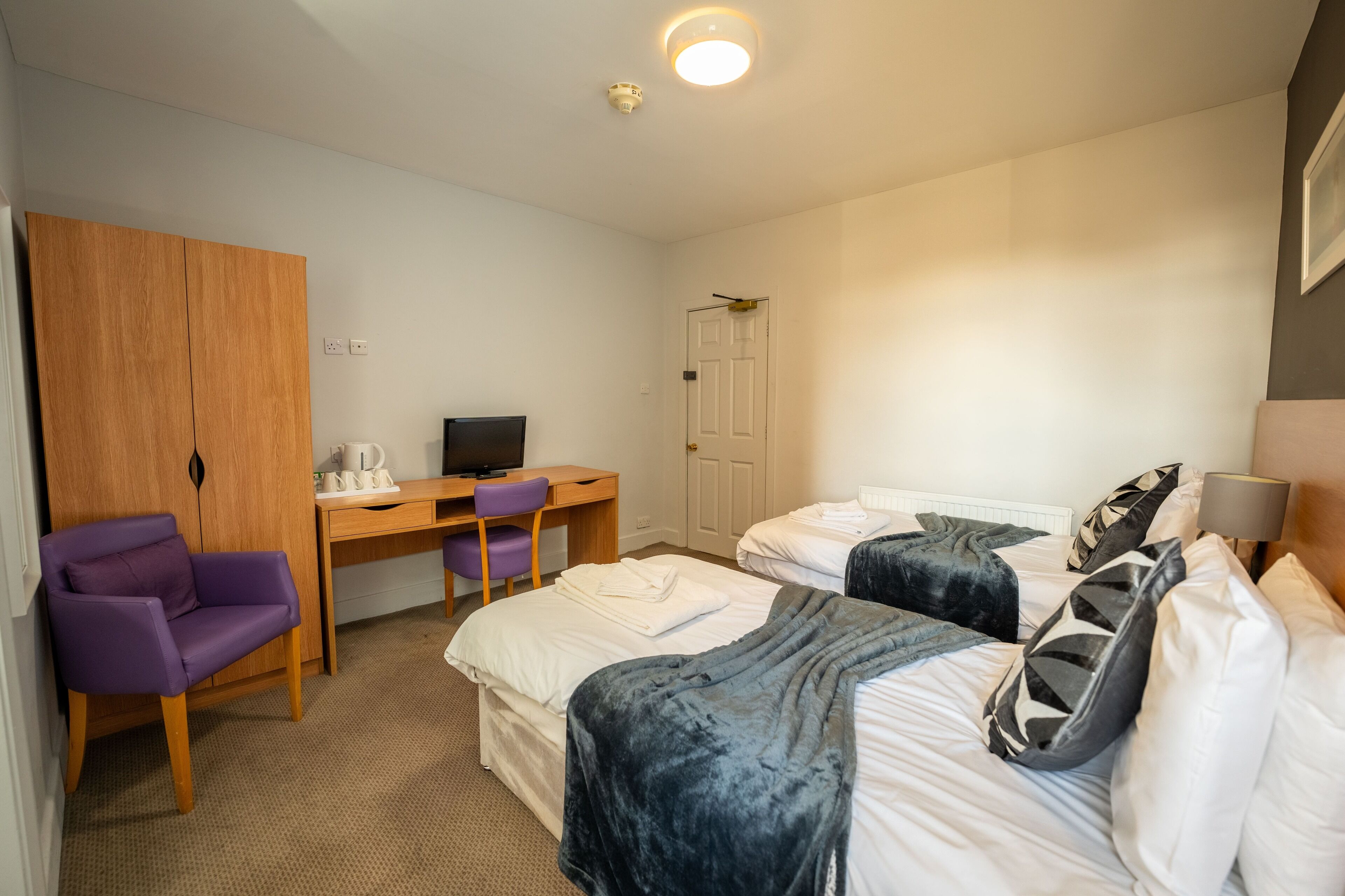 A hotel room with two beds, a desk, a chair, a wardrobe, and a television.