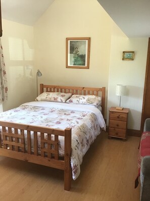 Un dormitorio con una cama de madera, ropa de cama floral, una mesita de noche, una lámpara y un cuadro en la pared.