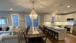 Una cocina moderna con armarios blancos, una isla central y un comedor con mesa y sillas de madera.