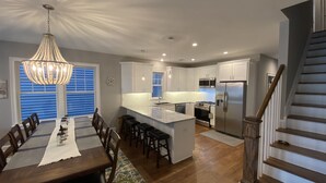 Una cocina moderna con armarios blancos, electrodomésticos de acero inoxidable y una mesa de comedor de madera con taburetes de bar.