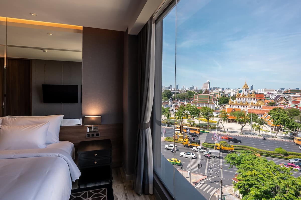 A hotel room with a large window, a bed, a TV, and a nightstand.