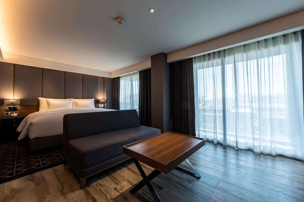 A modern hotel room with a bed, sofa, and a small wooden table.