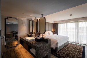 Una habitación de hotel moderna con una cama grande, un tocador de mármol y un espejo amplio.