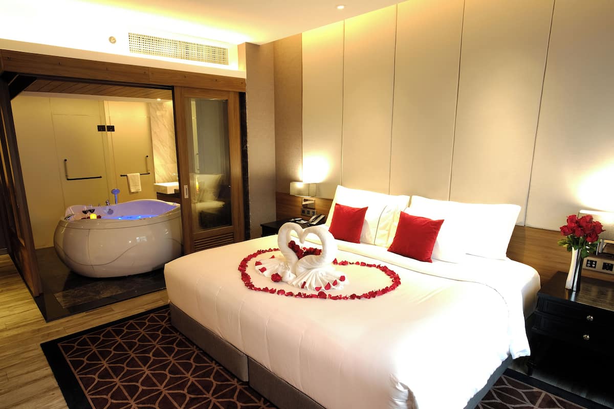 A hotel room with a large bed, a bathtub, and a mirror.