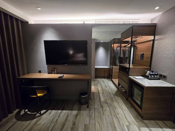 A modern hotel room with a flat-screen TV, wooden desk, chair, and a walk-in closet with a mirror. - Ayathorn Bangkok (Bangkok)