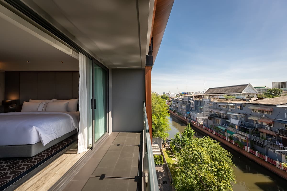 A balcony with a bed, a view of a canal, and traditional buildings in the background.
