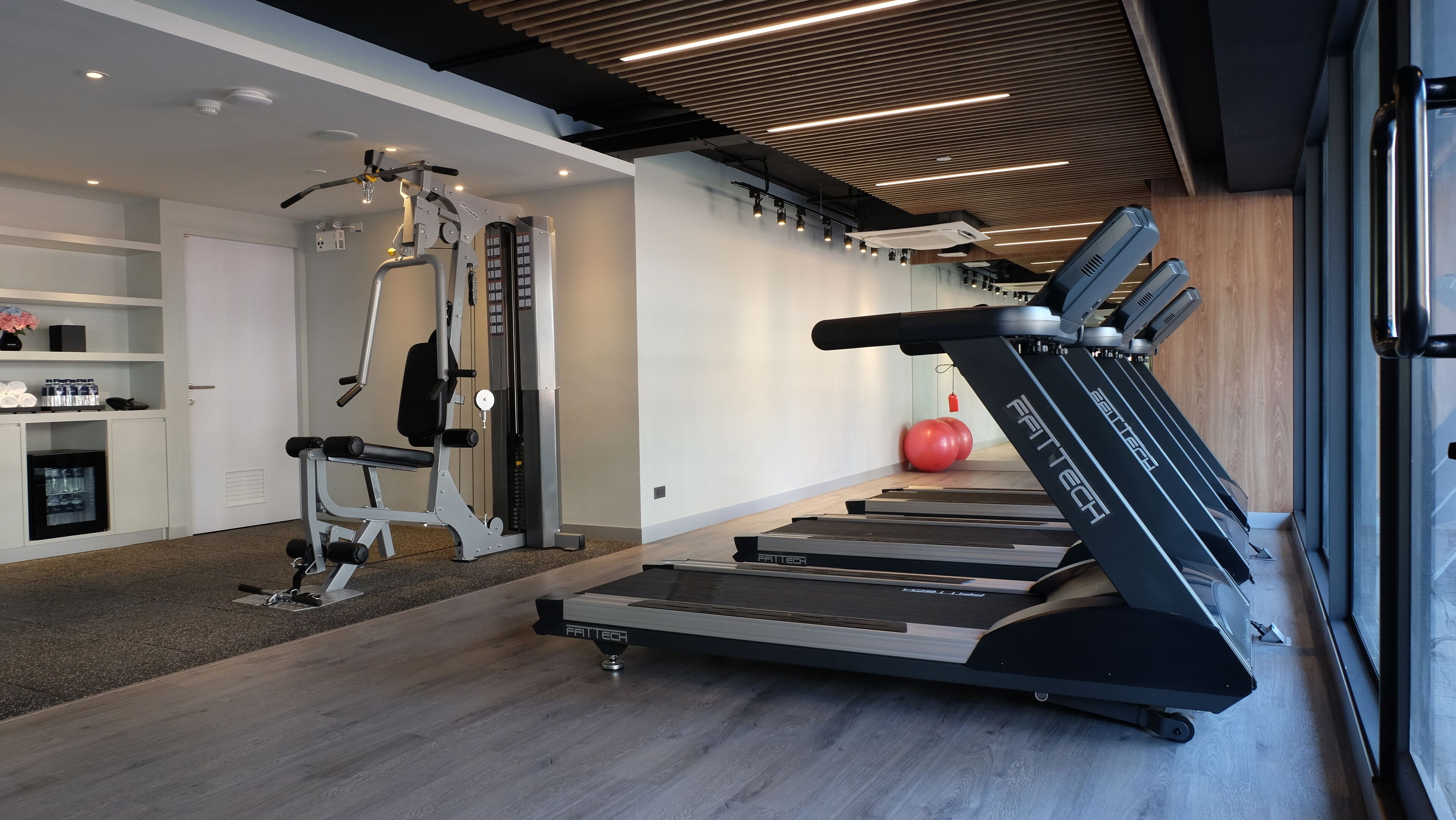 Un gimnasio moderno con cintas de correr, una máquina de pesas y una pelota de ejercicio roja.