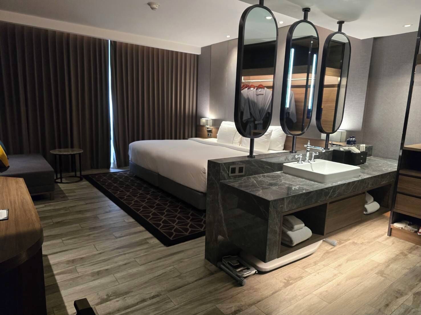 A modern hotel room with a large bed, a marble bathroom vanity, and a large mirror.