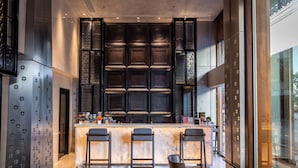 A modern kitchen with a marble countertop, three bar stools, and a large window.