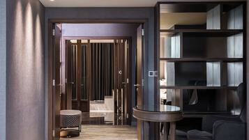 Een moderne hotelgang met een houten vloer, een zithoek met een ronde tafel en een grote boekenkast.