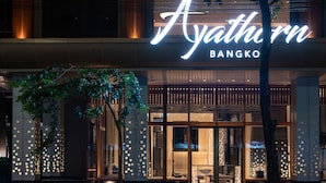 The exterior of Ayathorn Bangkok with illuminated signage, traditional decor, and a modern facade.