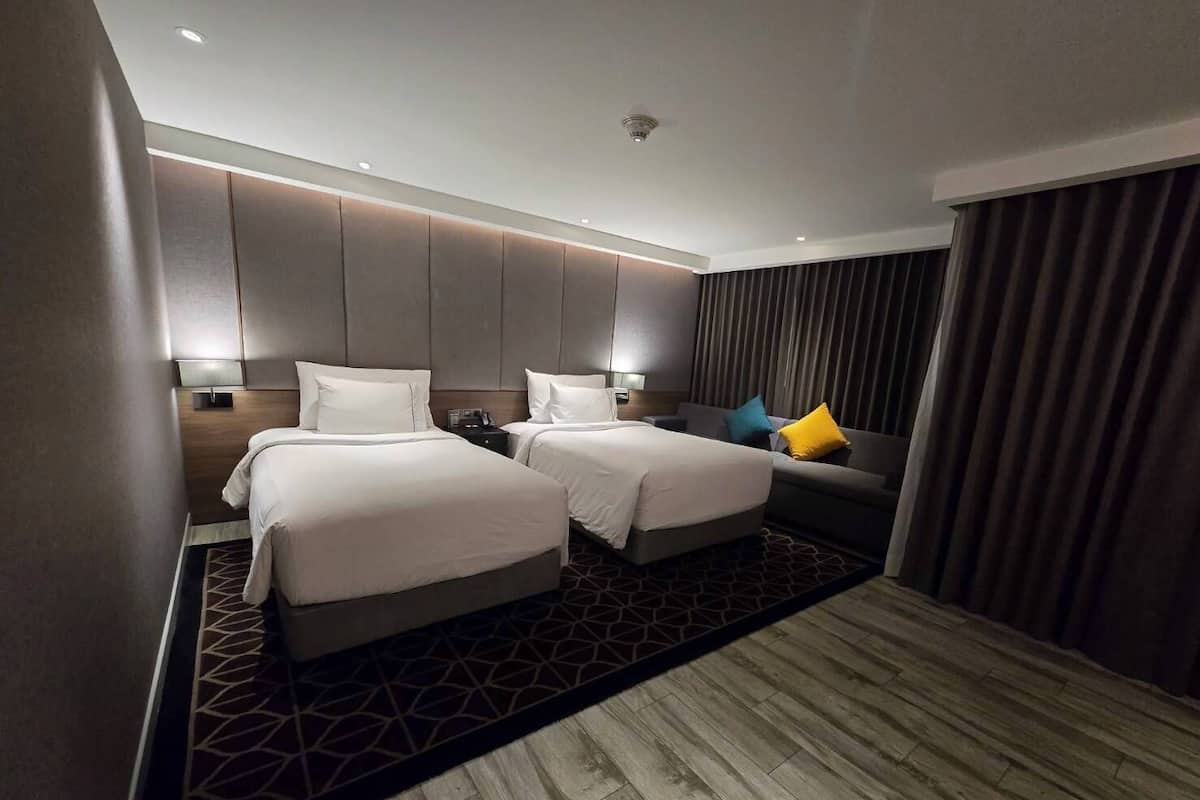A hotel room with two beds, a sofa, a patterned rug, and a ceiling light.