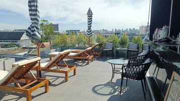 A rooftop terrace with wooden lounge chairs, a small round table, and striped umbrellas.