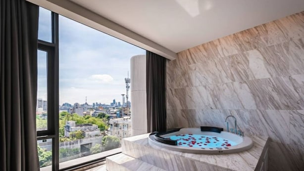 A modern bathroom with a marble floor, a bathtub with rose petals, and a city view through large windows.