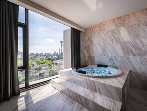 Une salle de bain moderne avec un sol en marbre, une baignoire remplie de pétales de roses et une vue sur la ville à travers de grandes fenêtres.