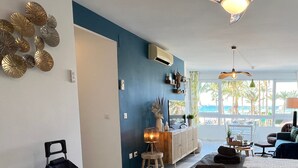 Un salon moderne avec un mur d’accent bleu, un meuble en bois, un canapé et une vue sur la plage grâce à de grandes fenêtres.