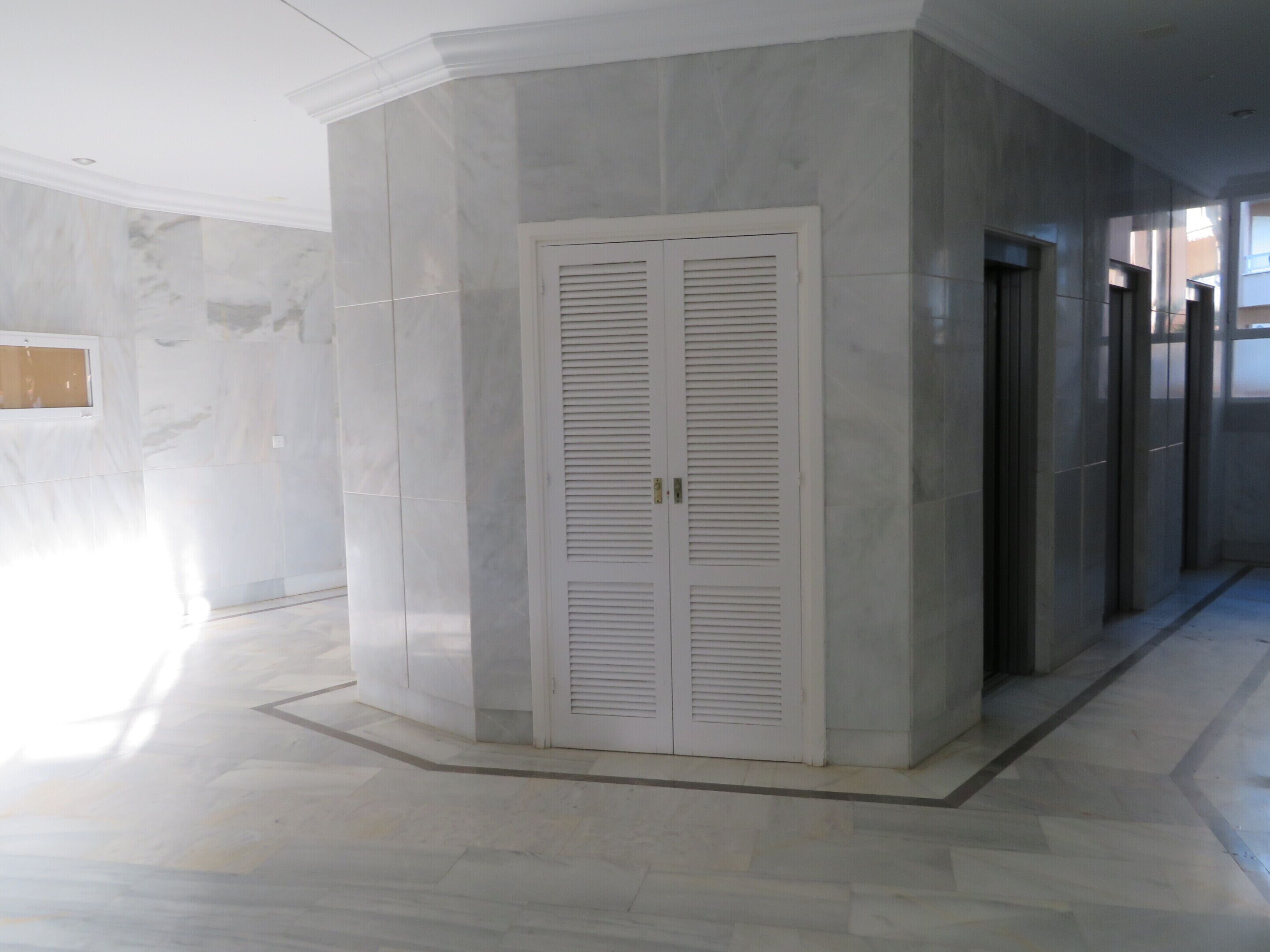 A corridor with a white louvered door, marble flooring, and a modern architectural design.