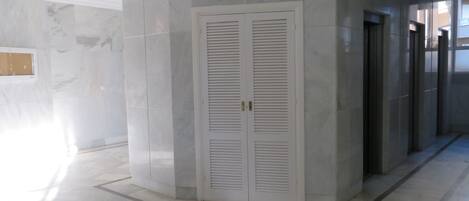 A corridor with a white louvered door, marble flooring, and a modern architectural design.