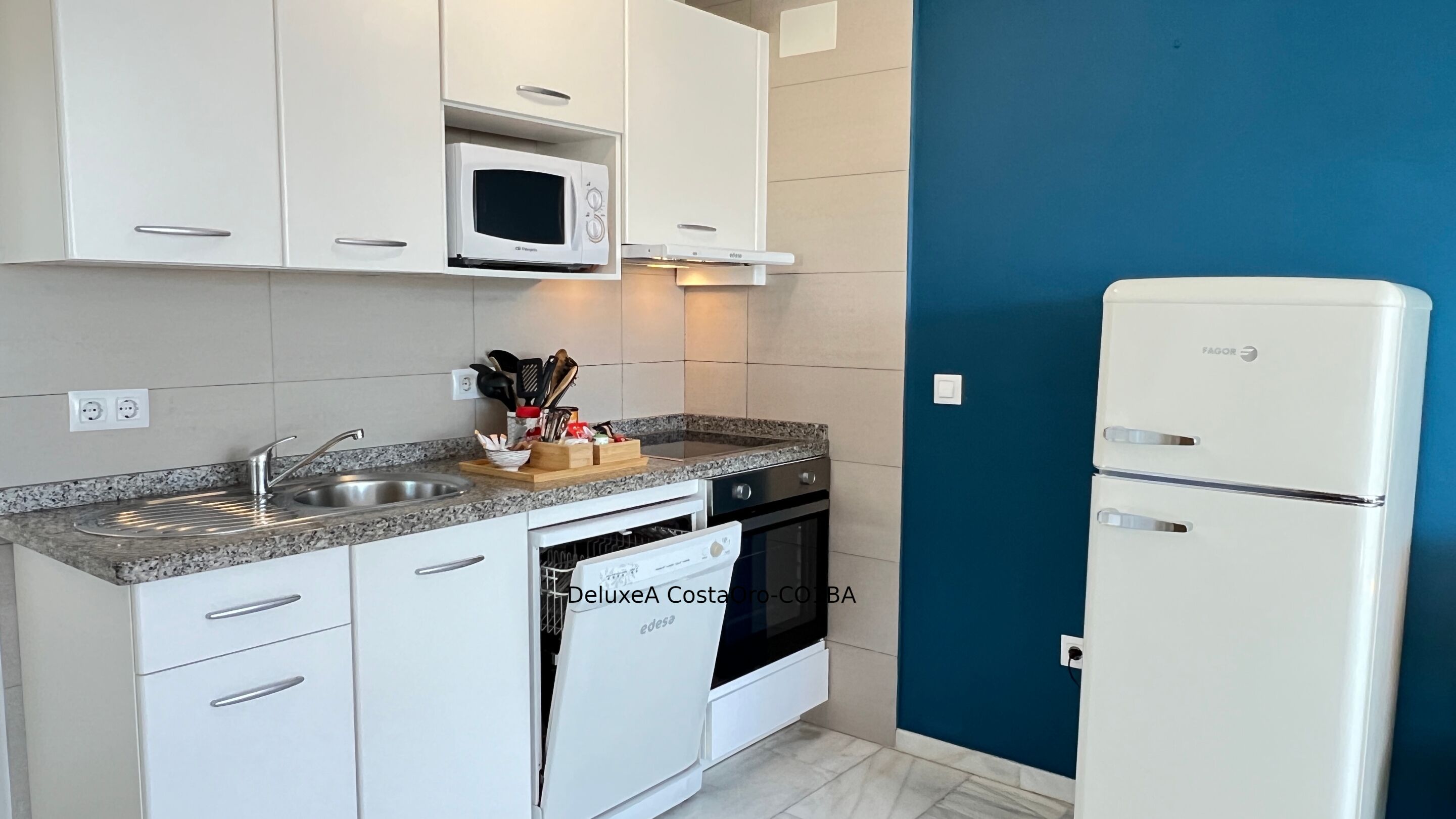 A modern kitchen with white cabinets, a built-in microwave, a stainless steel sink, a stove, and a white refrigerator.