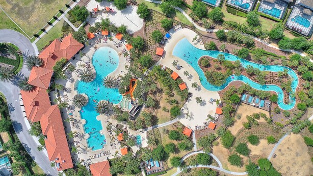 An aerial view of a resort with multiple swimming pools, palm trees, and a winding water feature.