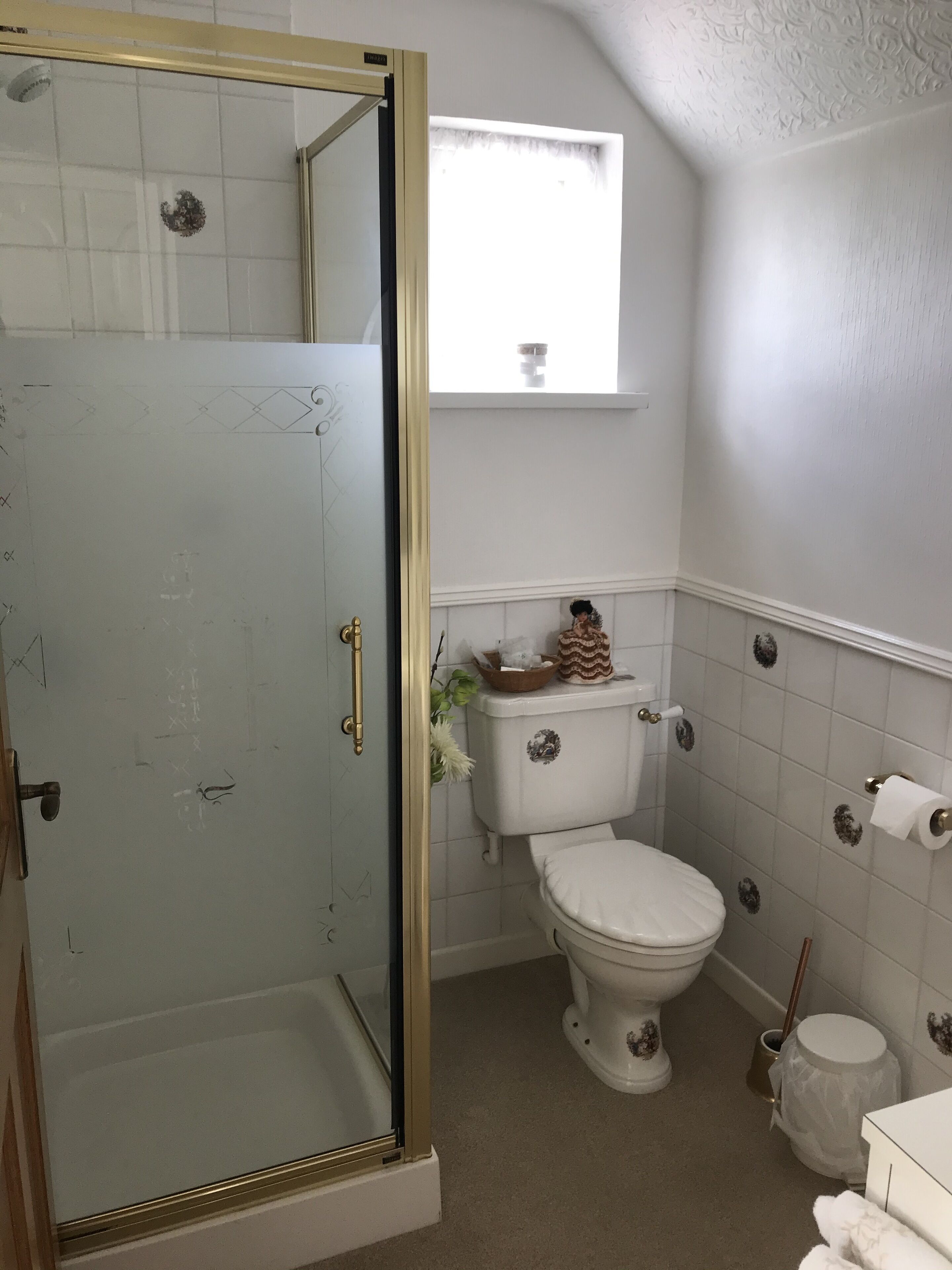 Een badkamer met een douchecabine van glas, een toilet en een raam boven de wastafel.