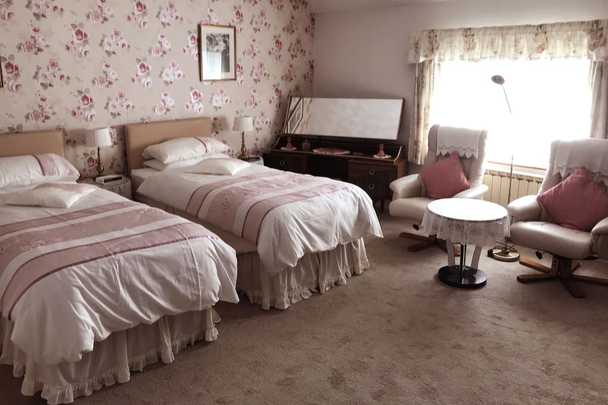 A bedroom with two beds, a chair, a small table, and a radiator.