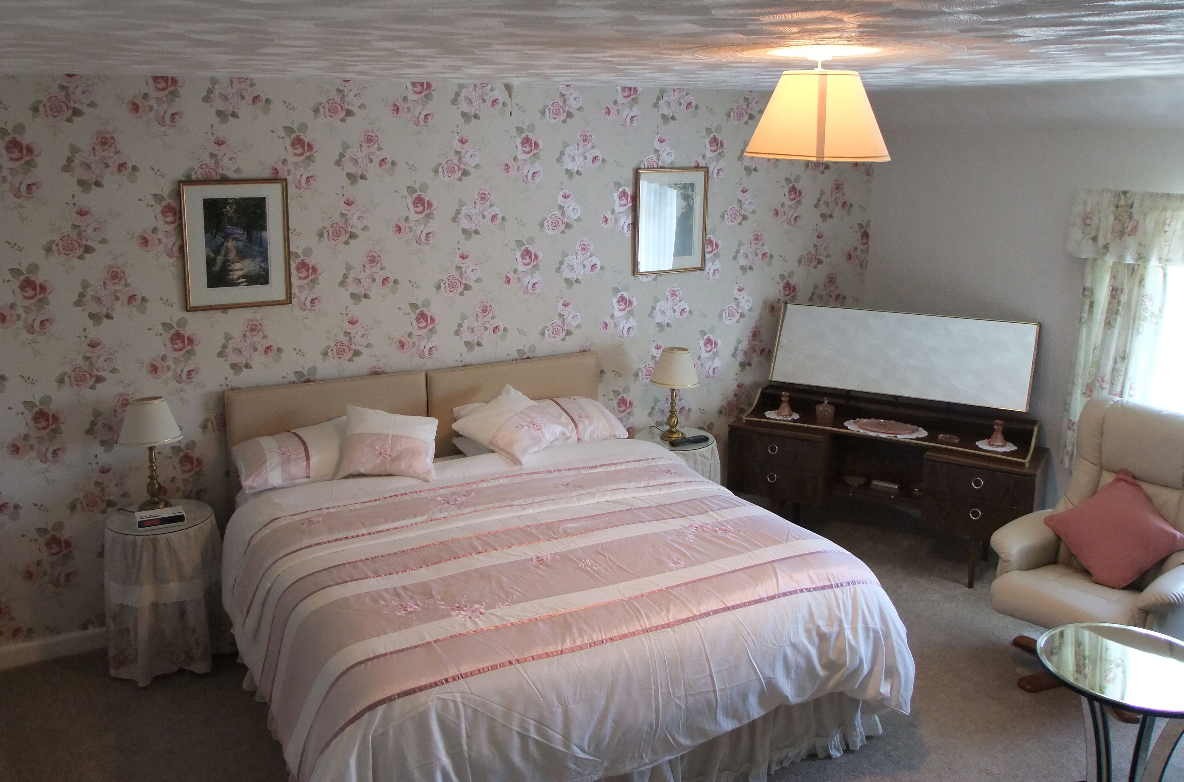 A bedroom with a bed, bedside tables, a chair, a dresser, and floral wallpaper.