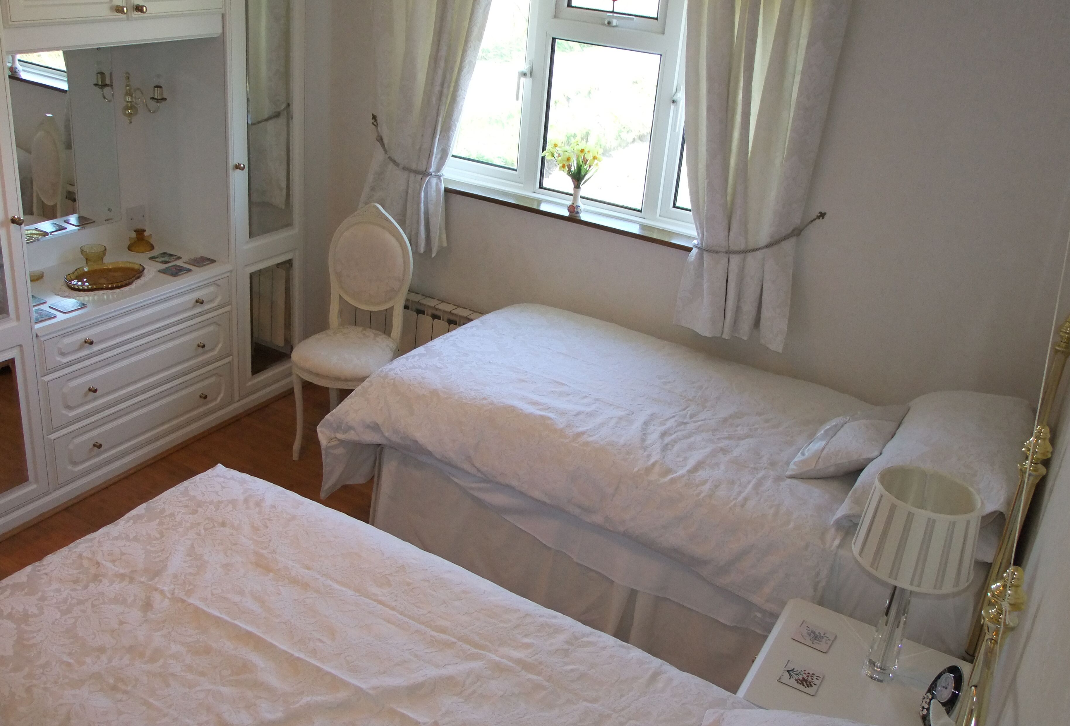A bedroom with two beds, a dresser, a chair, and a window with curtains.