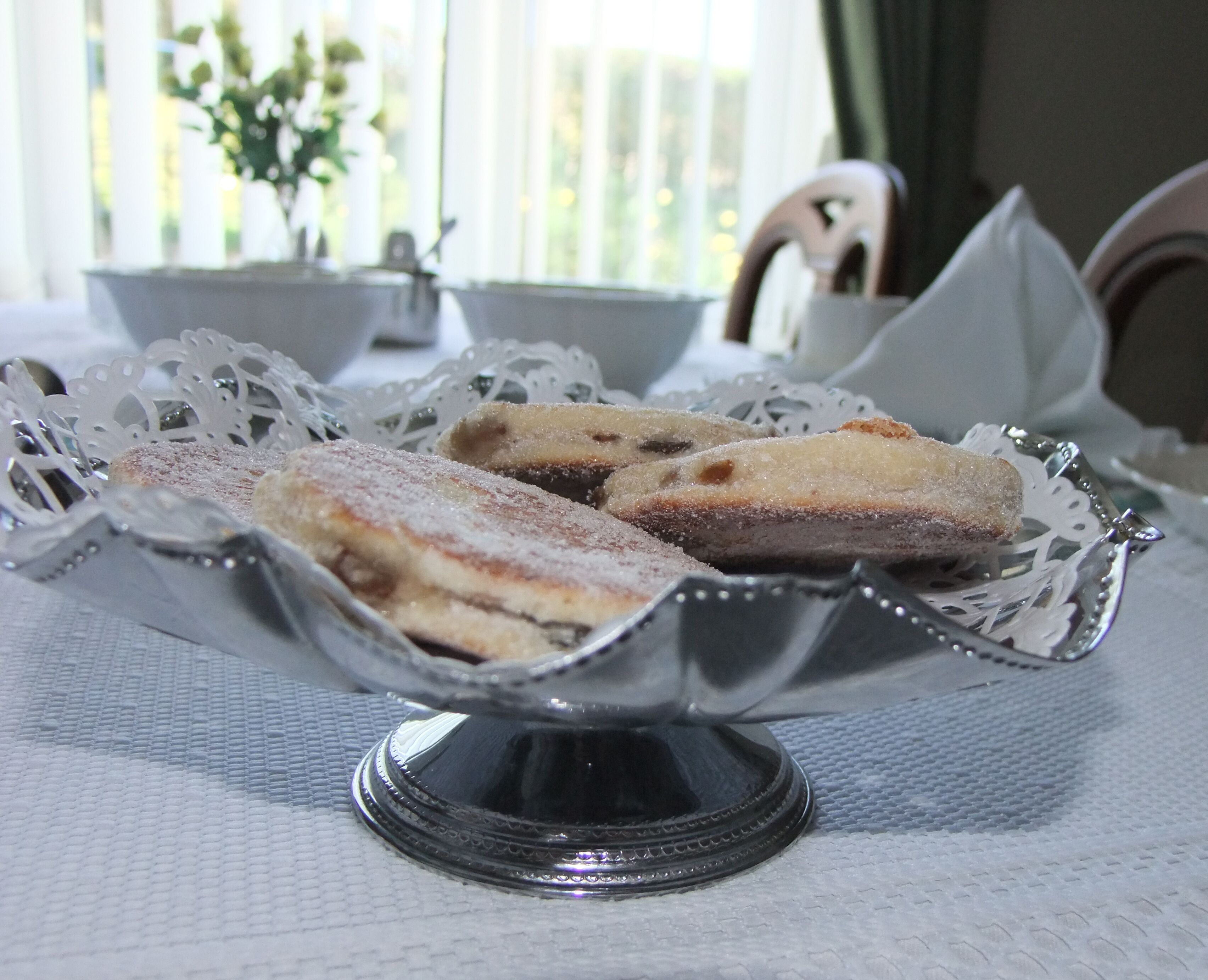 A silver dessert bowl with a lace doily on a textured tablecloth.
