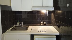 A kitchen with white cabinets, a stainless steel sink, a stove, and black tiled backsplash.
