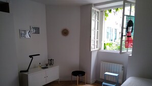 A bedroom with a bed, a desk, a radiator, a window, and a view of the outside.