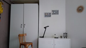 A room with a wooden chair, a white cabinet with two doors, and a desk with a lamp.