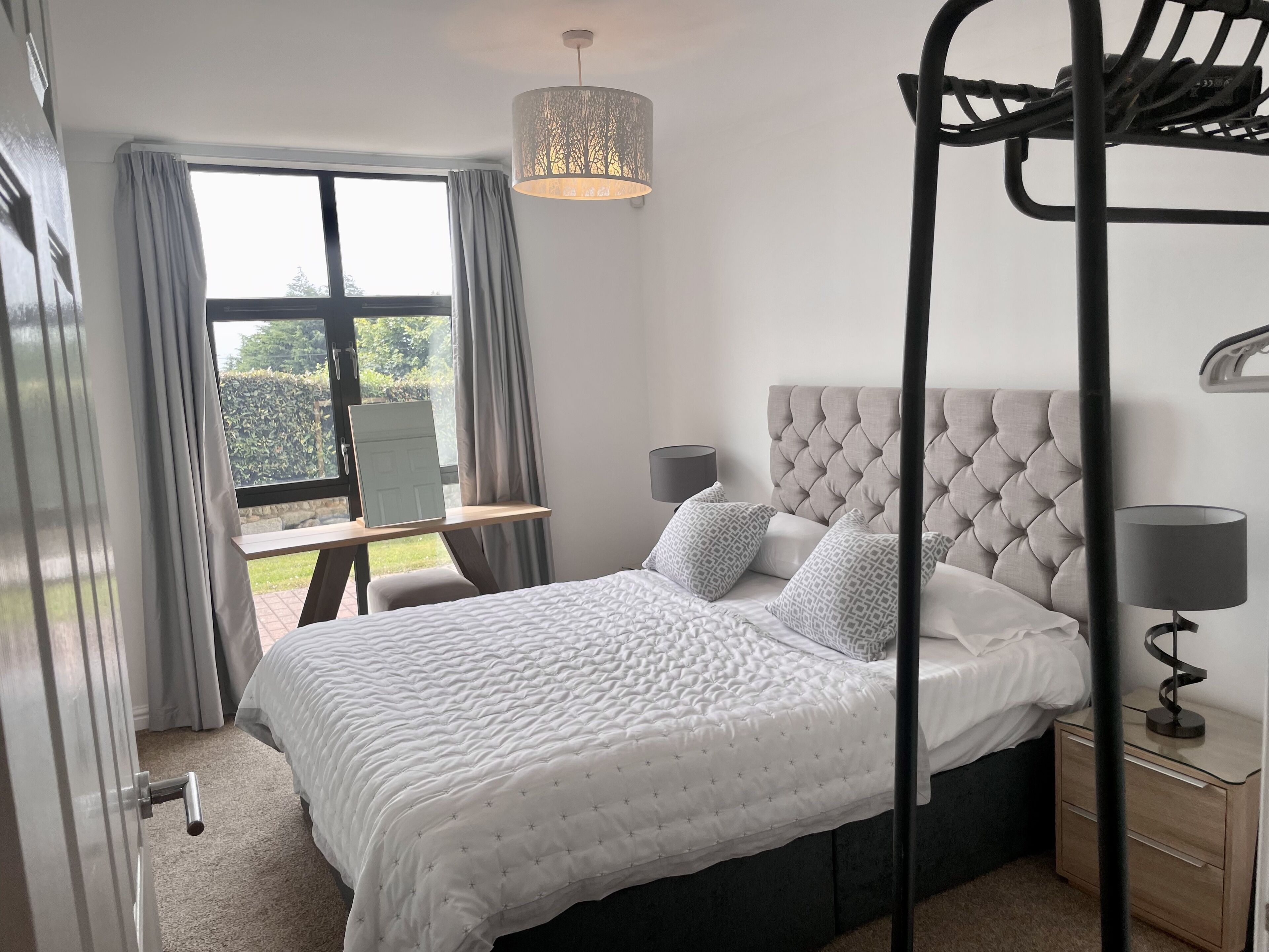 Une chambre à coucher avec un lit, des tables de chevet, un luminaire suspendu et une vue sur l’extérieur.