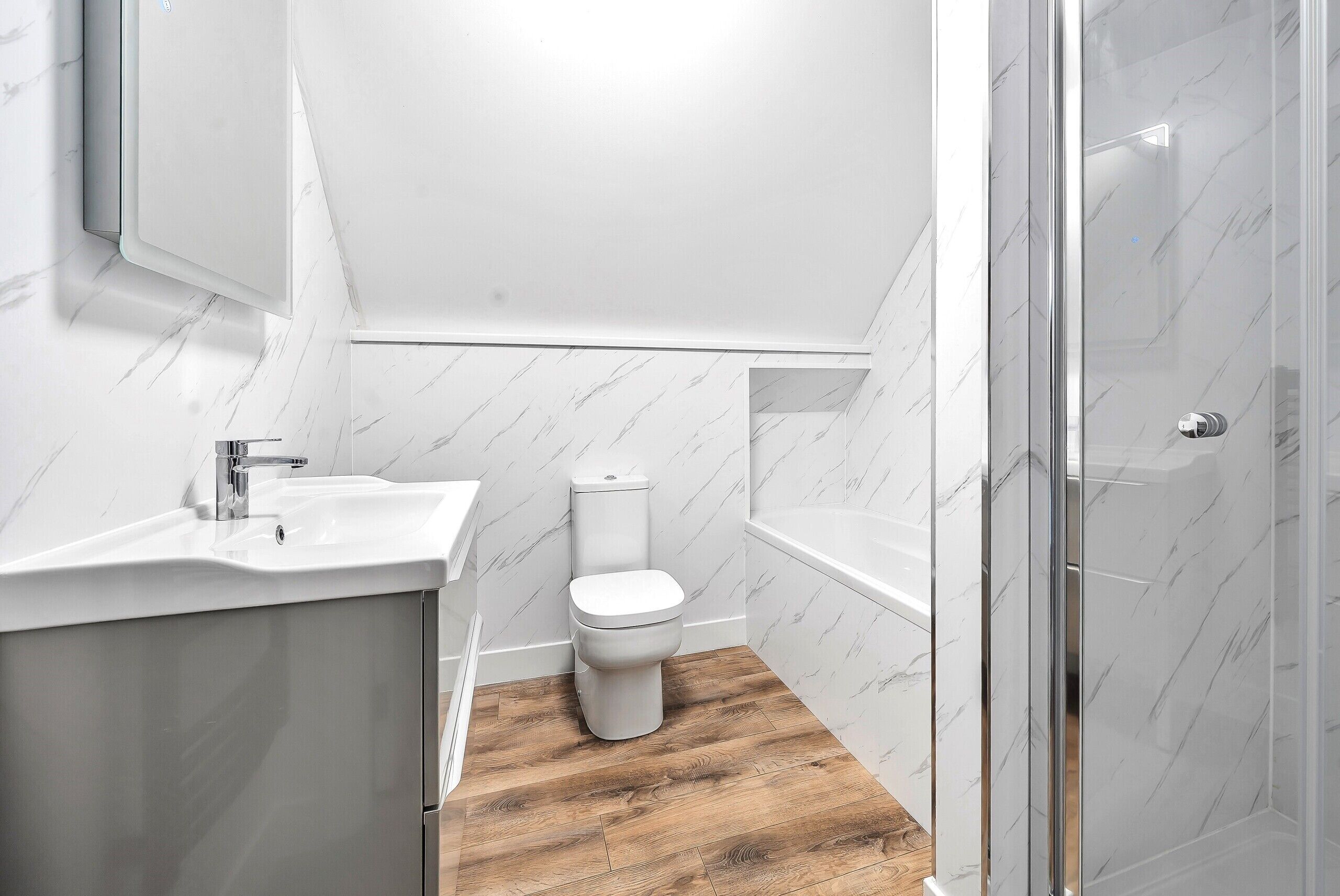 Une salle de bain moderne avec des toilettes blanches, un lavabo et un espace douche.