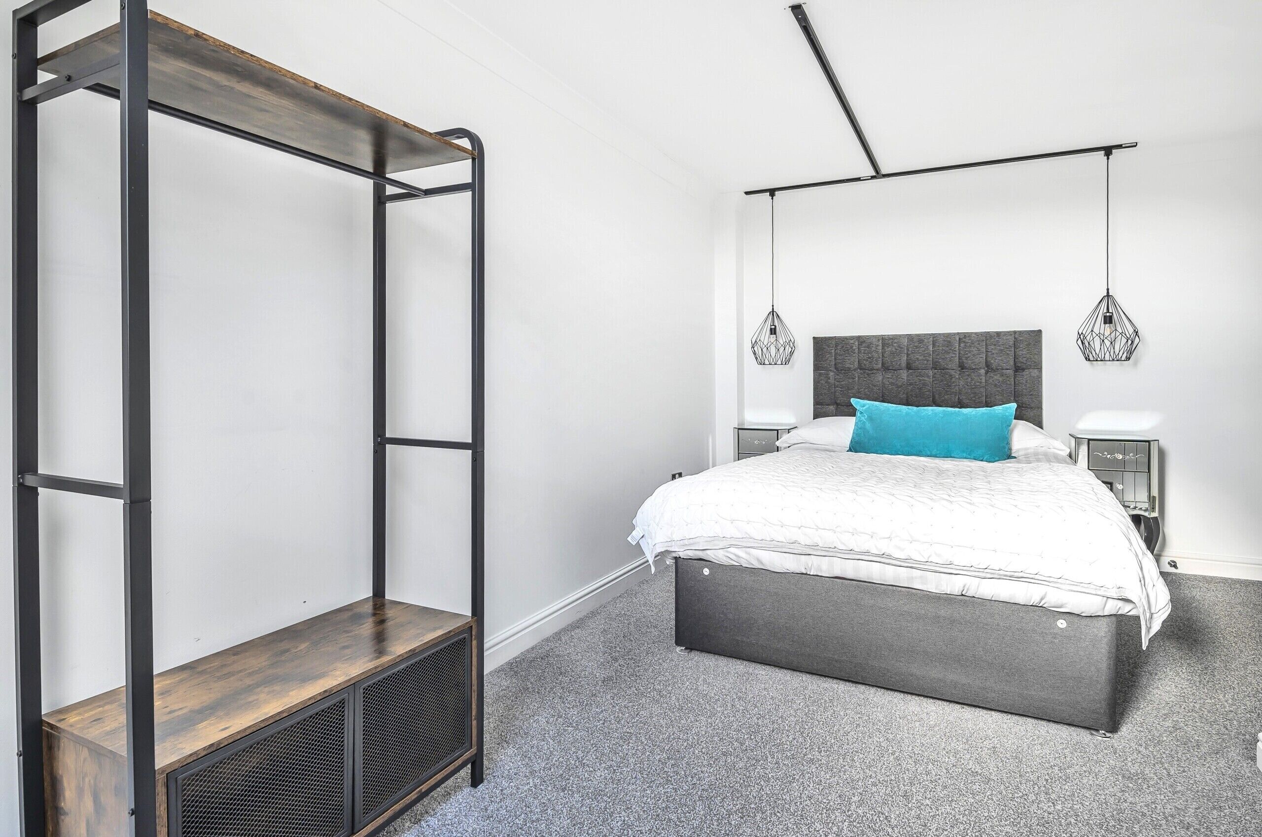 Un dormitorio con una cama, una mesita de noche, una lámpara colgante y una estantería metálica.