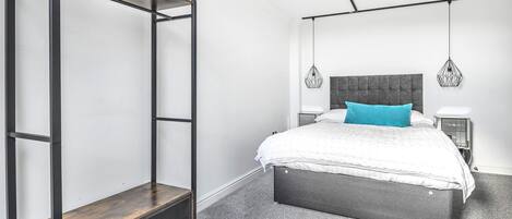 Un dormitorio con una cama, una mesita de noche, una lámpara colgante y una estantería metálica.
